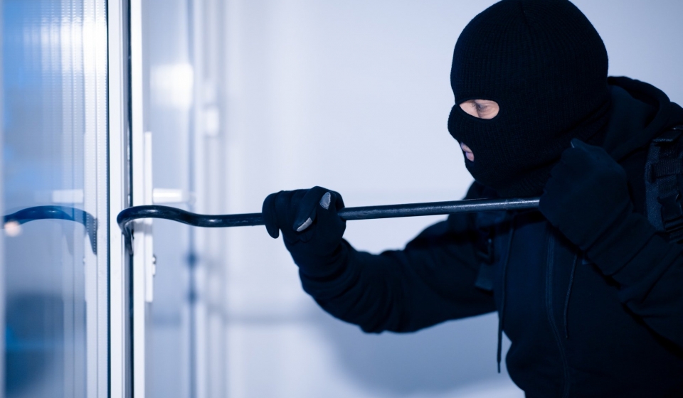 Robber in black balaclava cracking door with crowbar